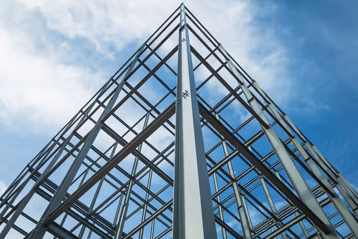 Structural steel framework of a building seen from below against a blue sky.